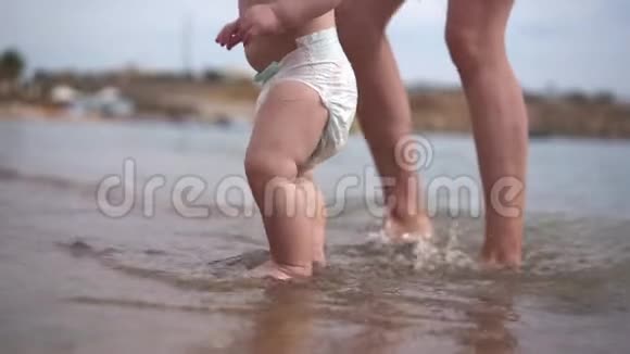 年轻的母亲和小孩子的腿慢慢地站在海里视频的预览图