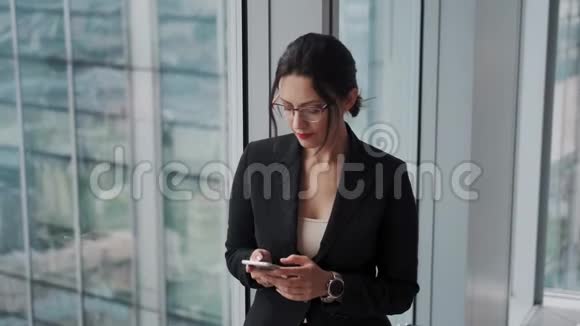 一位漂亮的女商人的肖像她手里拿着一部智能手机在一间现代化的办公室里视频的预览图