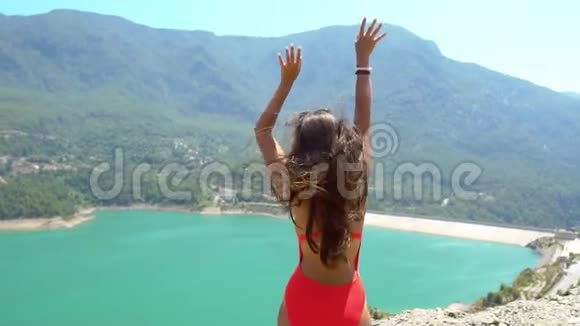 穿着泳衣的女人在夏日美丽的山湖上的岩石上跳舞视频的预览图