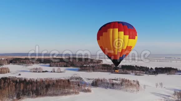 空中拍摄的人们乘坐一个明亮的大气球飞越冬季森林推拉缩放效果视频的预览图