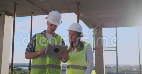 专业工程师穿着安全背心和头盔工作与数字平板和蓝图视频的预览图