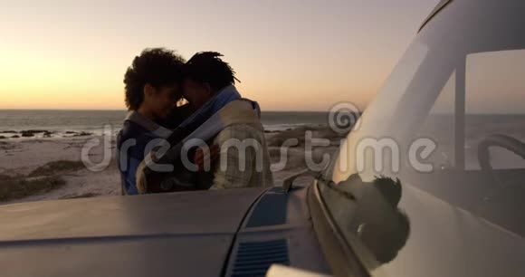 日落时分在海滩上的小货车旁裹着毯子的情侣视频的预览图