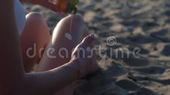 穿白色泳衣的年轻女孩在他的腿上擦防晒霜视频的预览图