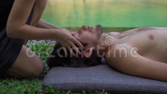 一位女治疗师在私人别墅的游泳池旁为一个年轻人做按摩的特写镜头家庭按摩视频的预览图