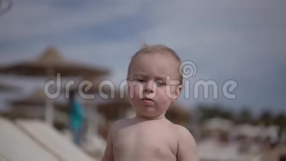 可爱的金发孩子一张严肃的脸站在海滩上看着大海视频的预览图