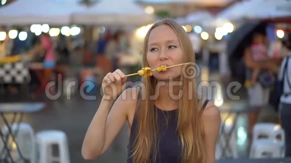 一名年轻女子在亚洲街头市场吃街头食品的慢镜头视频的预览图