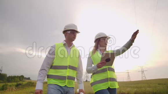 两位工程师一男一女戴着头盔带着一块石碑的工程师在电塔上行走讨论视频的预览图