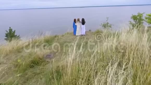 在湖边或河边散步的三个穿着夏日长礼服的女朋友的空中景色两名白种人和一名白种人视频的预览图