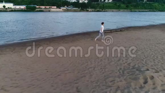 日落时女人沿着河的沙滩奔跑美丽的城市景色视频的预览图