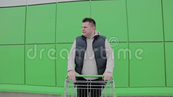 男人在停车场购物中心玩得开心快乐有趣的家伙骑在购物车上附近有购物手推车的顾客视频的预览图
