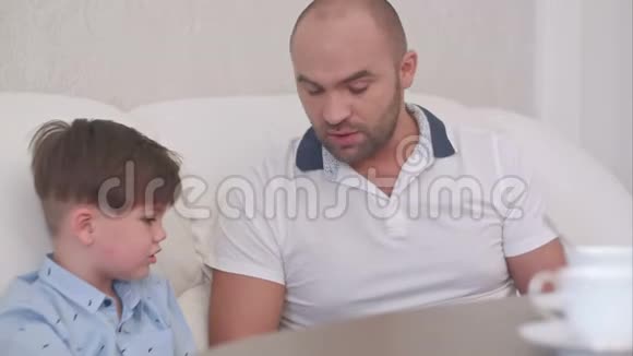 父子俩在家里的沙发上用数码平板电脑视频的预览图