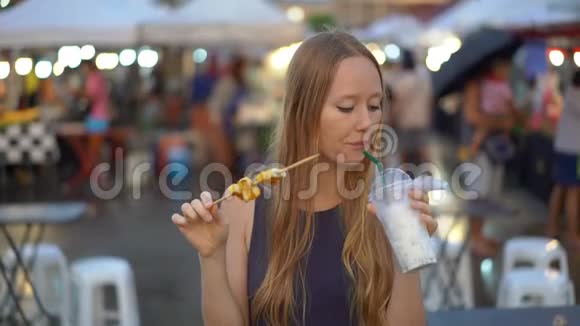 一名年轻女子在亚洲街头市场吃街头食品的慢镜头视频的预览图