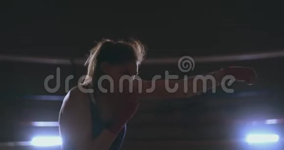 职业漂亮的女拳击手在黑暗的大厅里用蓝色的动作缓慢地展开了一场皮影戏视频的预览图