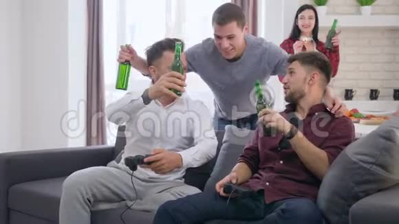 快乐的朋友一起在沙发上品尝啤酒瓶和玩电子游戏视频的预览图