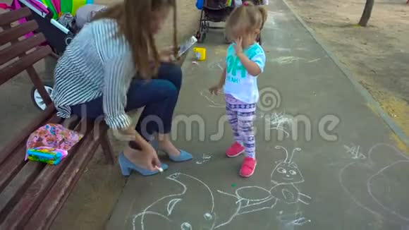 女孩在母亲附近的沥青上画画视频的预览图