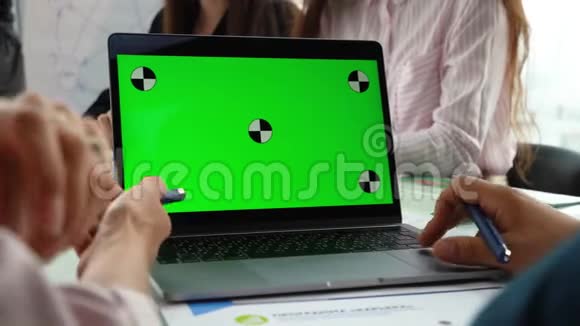 一个人的手在笔记本电脑上绿色屏幕上工作的特写在背景中人们坐在桌子旁视频的预览图