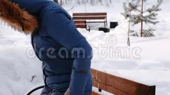 女人从长凳上站起来摇下雪和树叶冬季城市公园白天在下雪天气与视频的预览图