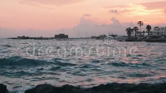 红色日落有暴风雨的大海码头长廊和地平线上的城堡塞浦路斯帕福斯日落时太阳路和海浪撞击岩石视频的预览图