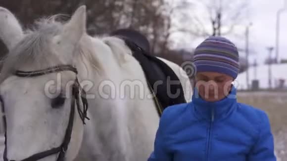 一个穿着夹克和帽子的年轻女人走了带着一匹白马去了马厩视频的预览图
