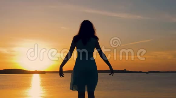 一个面对太阳的女人在日落时举起双手的剪影视频的预览图