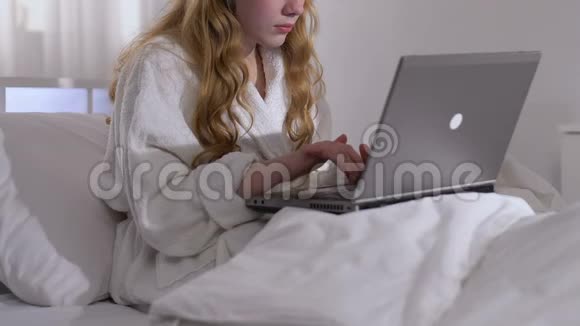 穿浴袍的女性自由职业者在床上打手提电脑远程访问工作视频的预览图