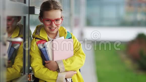 穿着黄色夹克和红色眼镜的女学生害羞地笑着看着镜头回到学校视频的预览图