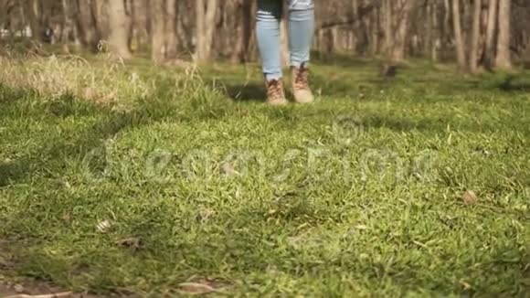 女人穿着牛仔裤和靴子腿走在明亮的绿色草地上视频的预览图