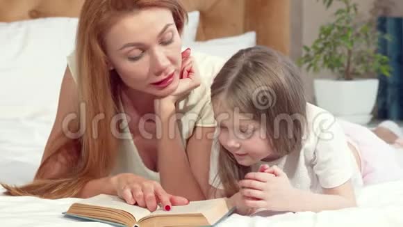美丽的女人和她可爱的小女儿一起看书躺在家里的床上视频的预览图