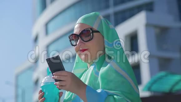 一位年轻的穆斯林妇女戴着浅色围巾和太阳镜戴着现代建筑的背景视频的预览图