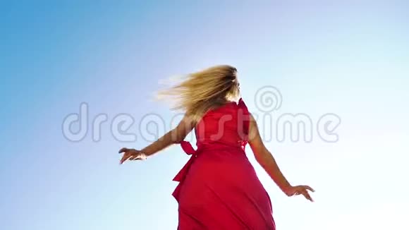 低角度拍摄性感金发女郎穿着红色连衣裙在背景上与蓝天共舞视频的预览图