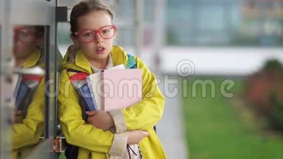 穿着红色眼镜和黄色夹克的疲惫女孩站在学校附近叹息学习负担上学困难视频的预览图