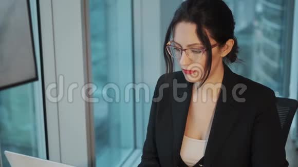 一位漂亮的女商人戴着眼镜在现代办公室的电脑上工作的画像视频的预览图