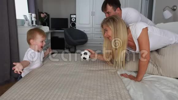 爸爸和妈妈在床上和男孩一起玩球视频的预览图