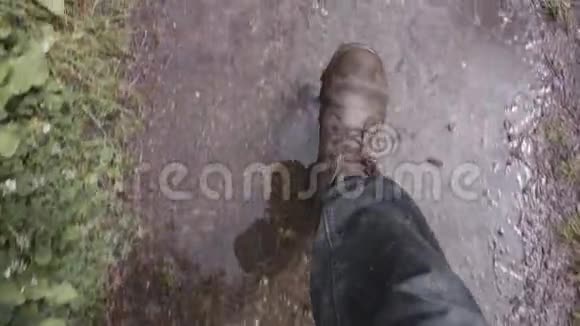 棕色靴子的徒步旅行者腿的顶部视图在水坑中行走透明的水和产生水溅股票视频的预览图
