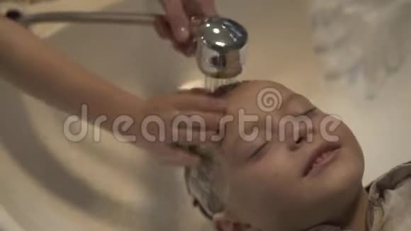 儿童发型师在理发店用洗发水给小男孩洗头在理发店关上洗小孩的头视频的预览图