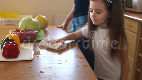 长发学龄前女孩用毛巾擦桌子妈妈和厨房里的小女孩妈妈助理教育视频的预览图