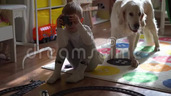 家庭生活方式一个小男孩在孩子们房间里玩玩具火车一只大狗看着它视频的预览图