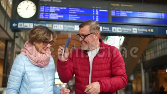 快乐的退休夫妇在火车站一个男人开玩笑地挥舞着护照和机票一个女人把它们拿在手里视频的预览图