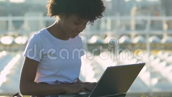 年轻的美国黑人妇女在电脑上工作坐在城市公园的草地上视频的预览图