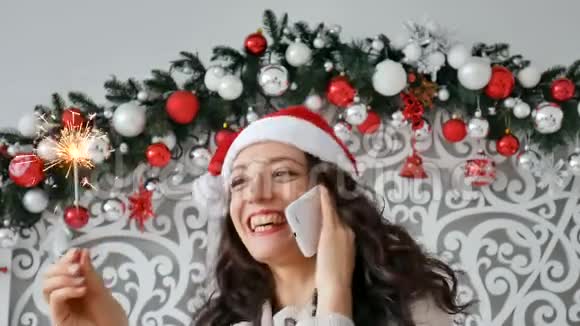 戴着圣诞帽的开朗深色卷发女士带着兴奋的表情在电话中交谈真诚地微笑模仿空间视频的预览图