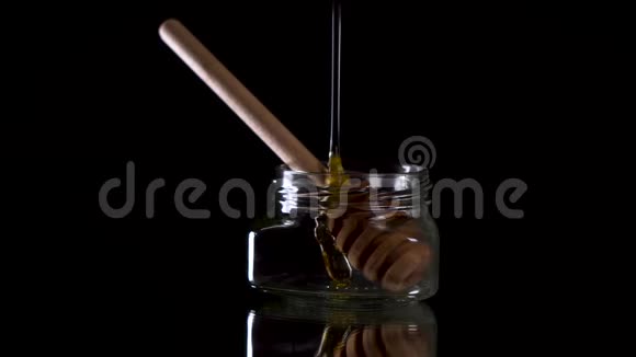 在透明的罐子里倒入蜂蜜蜂蜜勺子在黑色的背景上视频的预览图
