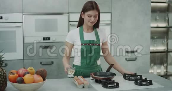 一个穿着绿色围裙的女孩在滚烫的平底锅里煮鸡蛋视频的预览图
