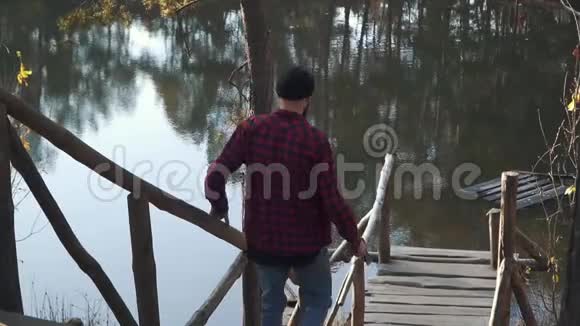 一个长着胡须的家伙手里拿着一把斧头走在桥边的湖边有胡子的年轻人在户外拿着斧头视频的预览图