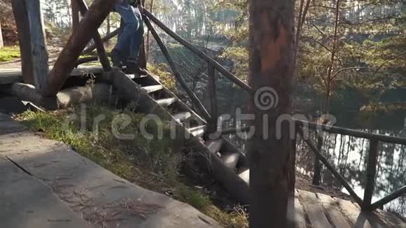 手里拿着斧子的大胡子走在靠近美丽森林和湖泊的木制楼梯旁一个长着胡子拿着斧头的年轻人视频的预览图