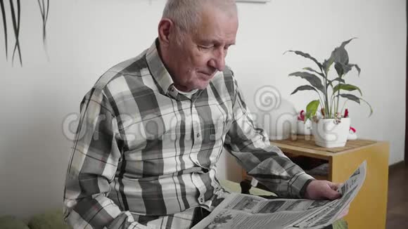 老人坐在椅子上在现代化的公寓里看报纸视频的预览图