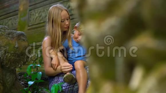 一名年轻女子和她的小儿子坐在乌布德的猴子森林生态公园的楼梯上慢镜头视频的预览图