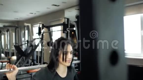 年轻的运动型黑发女孩准备用杠铃在蹲上做运动健身房的训练视频的预览图