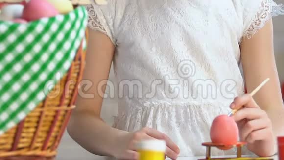 小女孩用油漆装饰彩蛋复活节礼篮站在桌子上视频的预览图