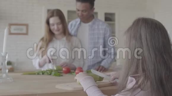 在现代厨房里一位非洲裔美国人和一位微笑的美女站在桌边做沙拉小女孩视频的预览图