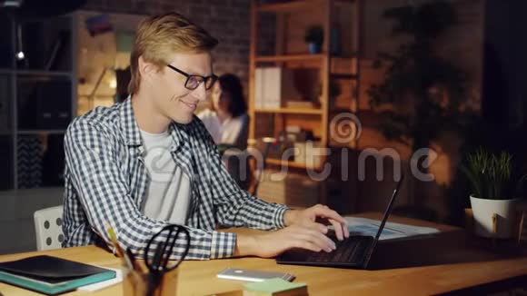 快乐的人在黑暗的办公室工作深夜用笔记本电脑微笑视频的预览图